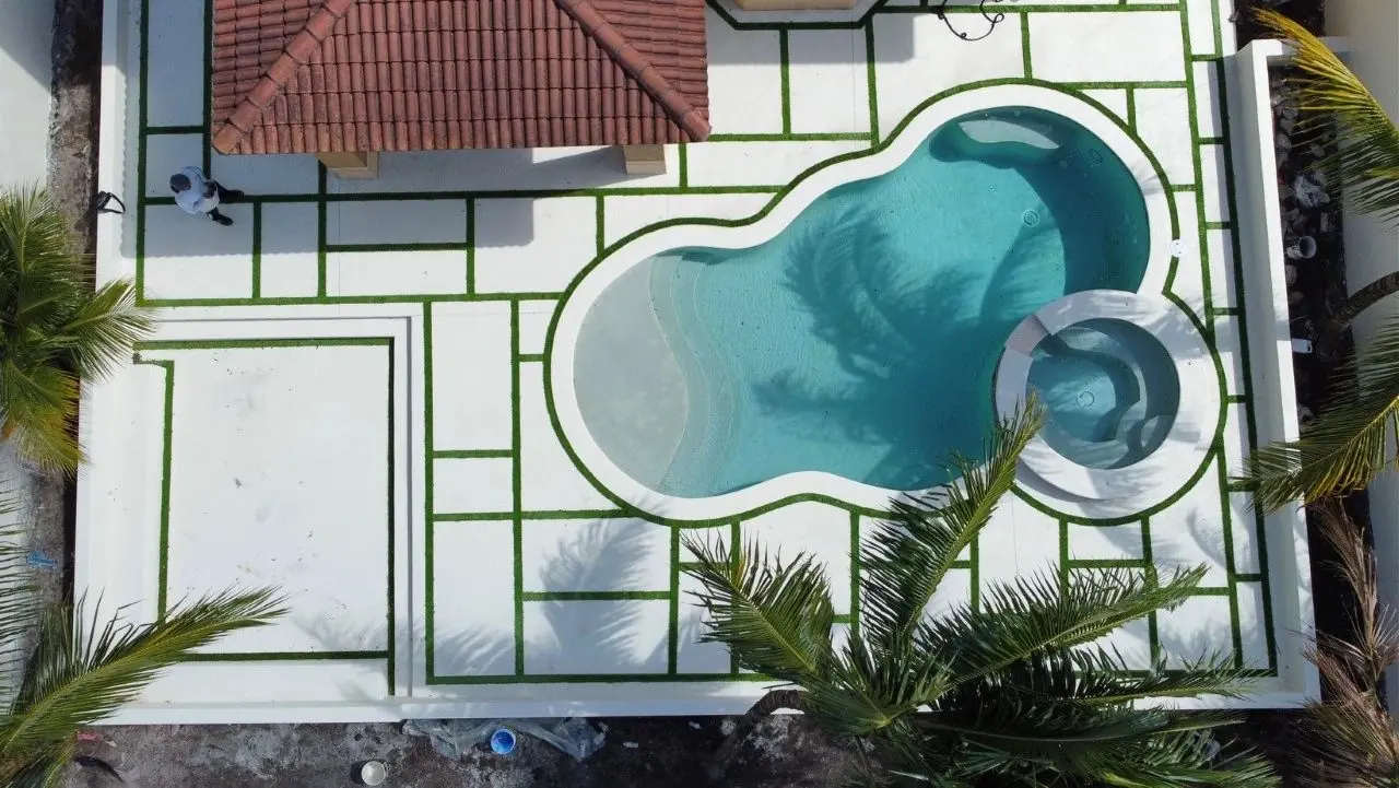 Aerial view of a freeform pool and spa with a white concrete deck and artificial grass joints
