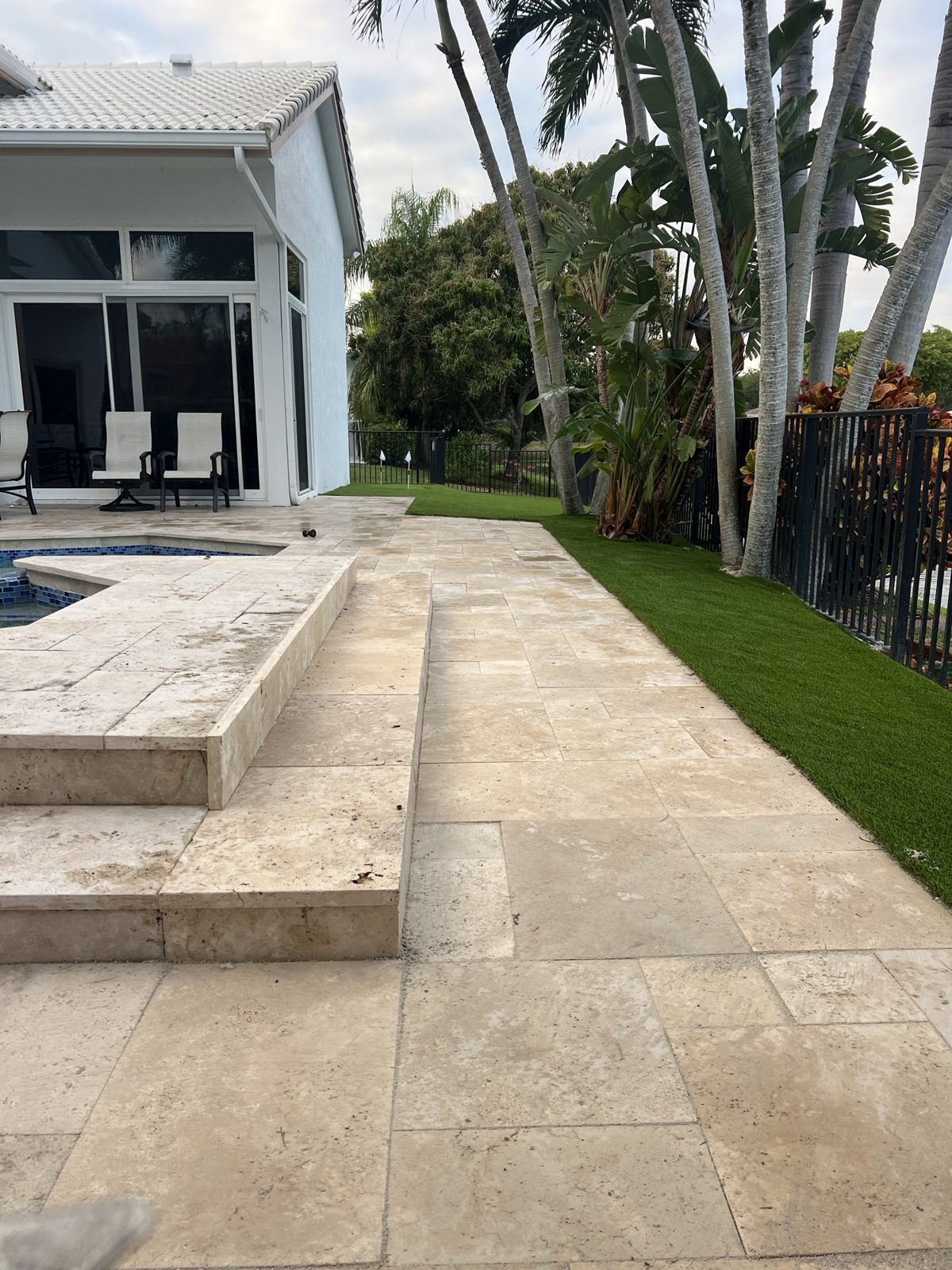 Travertine pool deck with a raised spa wall and artificial turf built by Concrete Solutions Today in Coral Springs, FL