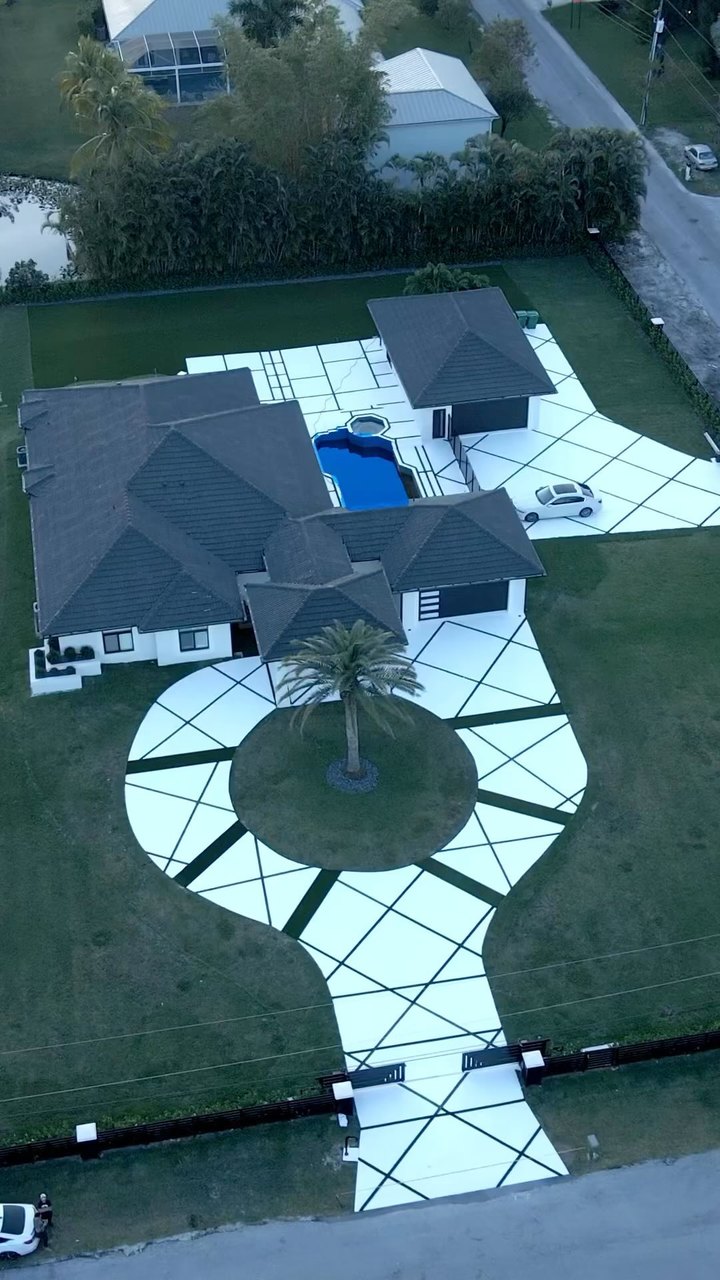 Aerial view of a Davie home with a circular concrete driveway, diagonal artificial grass lines, palm tree island, and pool deck