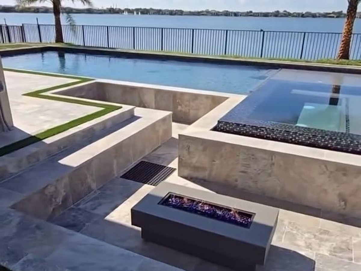 Lakefront pool deck in Parkland with a California-style sunken lounge, fire pit, raised spa, and artificial turf joints by Concrete Solutions Today