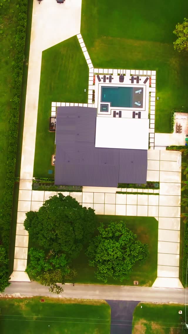 Aerial view of a Southwest Ranches estate with a long concrete and turf driveway, saltwater pool, natural stone deck, and aluminum pergola
